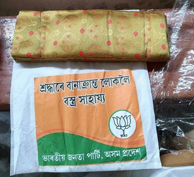 In the name of flood relief, the BJP is handing out polyester Mekhela Sadors ordered in bulk from factories in Surat, Gujarat while also doing their party advertisement at the same time